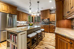Kitchen with brown cabinets, freestanding refrigerator, light wood finished floors, recessed lighting, and a kitchen island