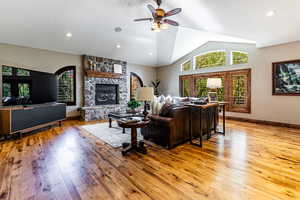 Living room featuring light wood finished floors, a ceiling fan, a stone fireplace, high vaulted ceiling, and recessed lighting