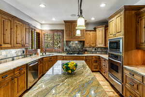 Kitchen featuring brown cabinets, light stone countertops, pendant lighting, and recessed lighting
