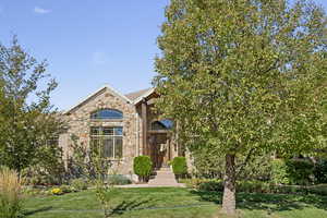 View of property hidden behind natural elements featuring a front lawn and stone siding