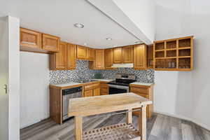 Kitchen featuring brown cabinetry, light countertops, decorative backsplash, stainless steel dishwasher, and recessed lighting