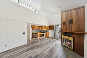 Unfurnished living room featuring a high ceiling, light wood finished floors, and a glass covered fireplace