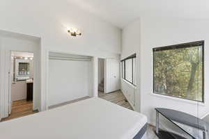 Bedroom featuring ensuite bathroom, light wood-type flooring, and a high ceiling