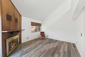 Unfurnished room featuring light wood finished floors, a large fireplace, and lofted ceiling