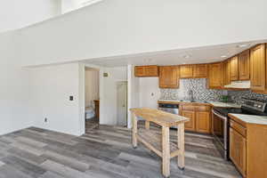Kitchen featuring appliances with stainless steel finishes, brown cabinetry, light countertops, tasteful backsplash, and dark wood-style floors