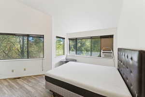 Bedroom featuring light wood finished floors, multiple windows, vaulted ceiling, and cooling unit