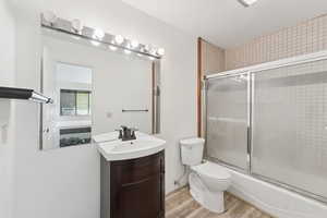 Full bathroom with light wood-style floors, vanity, bath / shower combo with glass door, and ensuite bath