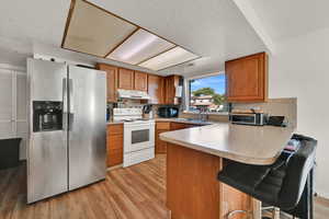 Kitchen with stainless steel fridge with ice dispenser, brown cabinets, a breakfast bar, a textured ceiling, and light wood-type flooring