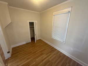 Unfurnished bedroom with wood finished floors, crown molding, and a closet