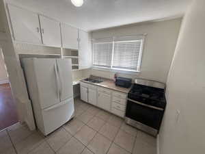 Kitchen featuring stainless steel range with gas stovetop, light countertops, freestanding refrigerator, and white cabinets
