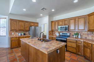 Kitchen with brown cabinetry, a textured ceiling, appliances with stainless steel finishes, backsplash, and recessed lighting