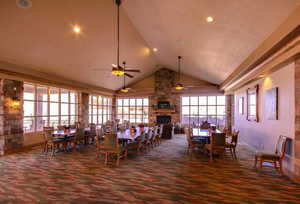 Dining area featuring dark colored carpet, high vaulted ceiling, a fireplace, ceiling fan, and plenty of natural light