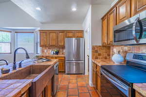 Kitchen with appliances with stainless steel finishes, brown cabinetry, tile countertops, a textured ceiling, and decorative backsplash