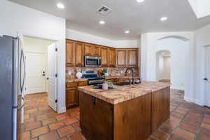 Kitchen featuring brown cabinets, recessed lighting, appliances with stainless steel finishes, arched walkways, and decorative backsplash