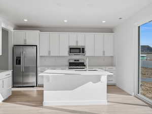 Kitchen with stainless steel appliances, white cabinets, a center island with sink, light wood-style flooring, and recessed lighting