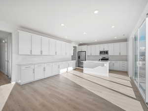 Kitchen featuring white cabinets, stainless steel appliances, light wood-type flooring, an island with sink, and recessed lighting