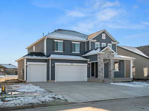View of front of home with a garage, concrete driveway, and stone siding
