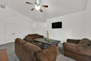 Carpeted living area with ceiling fan and high vaulted ceiling