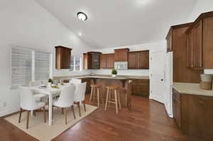 Kitchen and dining area with dark wood finished floors, a breakfast bar, glass insert cabinets, and high vaulted ceiling
