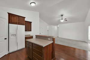 Kitchen featuring white fridge with ice dispenser, lofted ceiling, light countertops, dark wood finished floors, and open floor plan