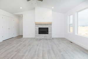 Unfurnished living room with lofted ceiling, light wood-type flooring, a stone fireplace, recessed lighting, and a ceiling fan