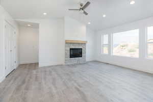 Unfurnished living room with lofted ceiling, light wood-style flooring, a stone fireplace, recessed lighting, and a ceiling fan