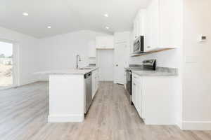 Kitchen featuring stainless steel appliances, white cabinetry, light wood-type flooring, light stone counters, and an island with sink