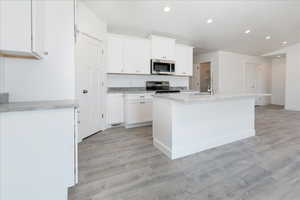 Kitchen featuring white cabinets, recessed lighting, a center island with sink, stainless steel appliances, and light wood-style floors