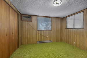 Basement with carpet flooring, a baseboard radiator, wooden walls, and a textured ceiling