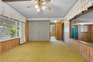 Carpeted spare room featuring wood walls and a ceiling fan