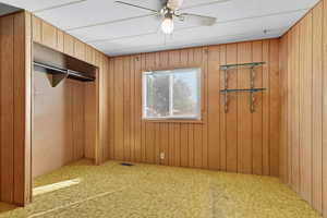 Unfurnished bedroom with ceiling fan, carpet, a closet, and wood walls