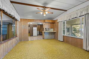Kitchen featuring wood walls, light colored carpet, light countertops, a peninsula, and freestanding refrigerator