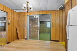 Unfurnished dining area featuring wood walls, wood finished floors, and a chandelier