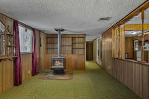 Unfurnished living room featuring wood walls, a wood stove, carpet floors, and a textured ceiling