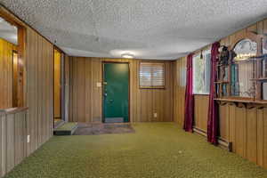Foyer entrance with wood walls, carpet flooring, a baseboard heating unit, and a textured ceiling