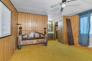 Carpeted bedroom with wood walls, multiple windows, and ceiling fan