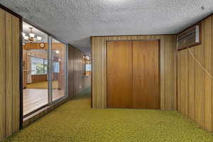 Hall with wood walls, carpet flooring, a chandelier, a textured ceiling, and a wall unit AC