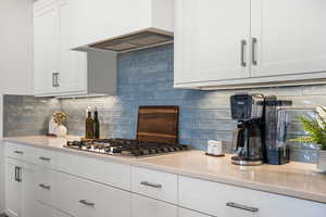 Kitchen featuring backsplash, white cabinets, custom exhaust hood, and stainless steel gas cooktop