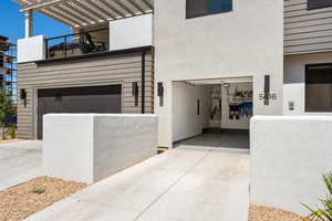 Property entrance with a pergola, an attached garage, concrete driveway, and stucco siding