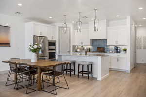 Kitchen with pendant lighting, white cabinets, appliances with stainless steel finishes, a kitchen bar, and a center island with sink