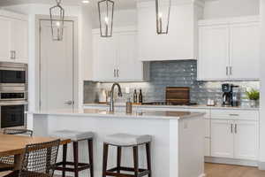 Kitchen featuring backsplash, white cabinets, stainless steel appliances, a breakfast bar, and a center island with sink