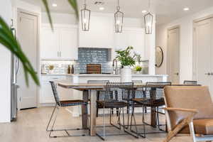 Kitchen with decorative backsplash, white cabinets, hanging light fixtures, an island with sink, and freestanding refrigerator