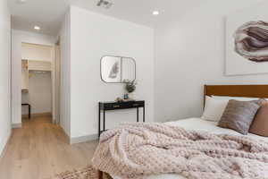 Bedroom with a spacious closet, light wood-type flooring, and recessed lighting