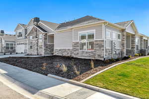 View of property exterior featuring stone siding, roof with shingles, a garage, and a lawn