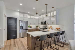 Kitchen featuring a breakfast bar, appliances with stainless steel finishes, glass insert cabinets, light wood-style flooring, and tasteful backsplash