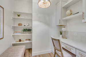 Office area featuring built in desk, light wood-type flooring, and a chandelier