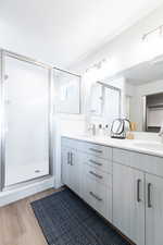 Bathroom with double vanity, a stall shower, and dark wood-style flooring