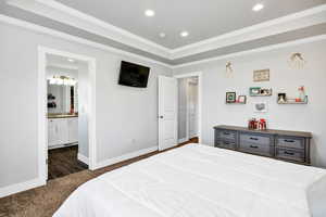 Primary bedroom with dark colored carpet, crown molding, a raised tray ceiling, recessed lighting, and ensuite bath
