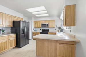 Kitchen featuring a peninsula, light countertops, fridge with ice dispenser, black range with electric cooktop, and stainless steel microwave
