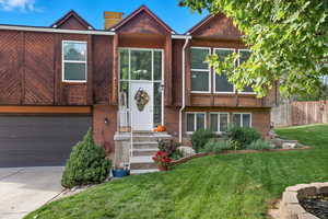 View of front facade with brick siding, an attached garage, concrete driveway, and a chimney